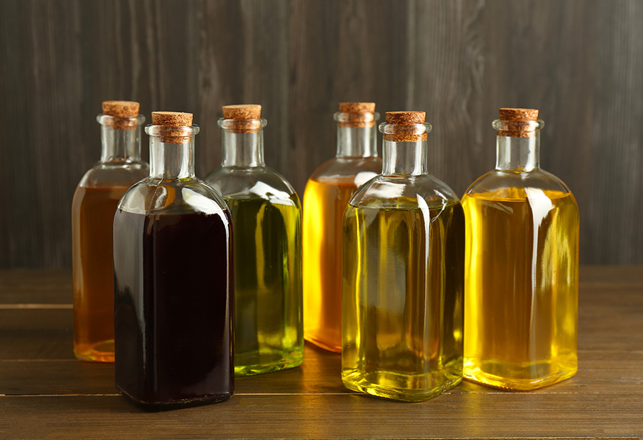 Different bottles of different colored oil on a wooden table.