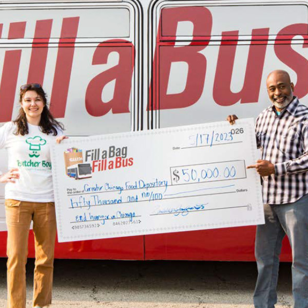 A man and a woman standing in front of a bus. They are holding a large check showing 50,000 dollars donated to greater Chicago food depository.