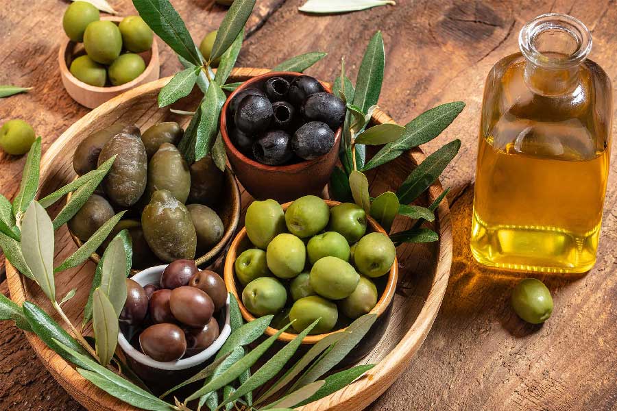 Close-up of a wooden bowl full of olives and an bottle full of oil on a wooden table