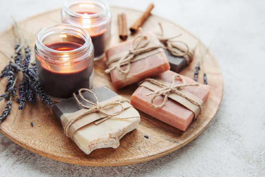 Two candles and various bars of soap sitting on a wooden serving tray