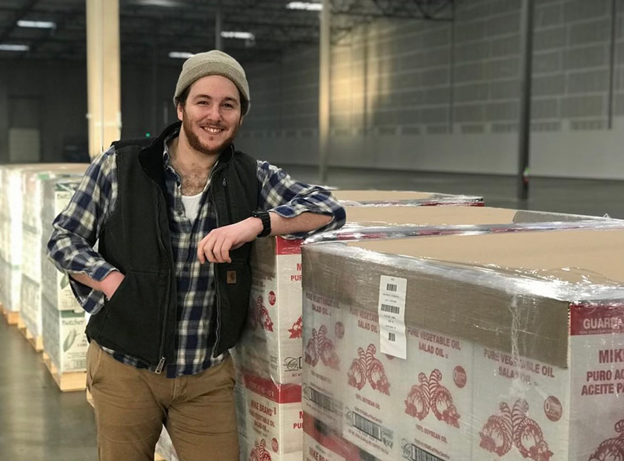 Ben Caffrey standing in a warehouse in front of pallets of Mike Brand branded boxes.